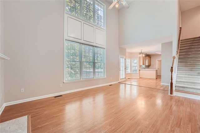 unfurnished living room featuring ceiling fan with notable chandelier, light hardwood / wood-style floors, and a high ceiling