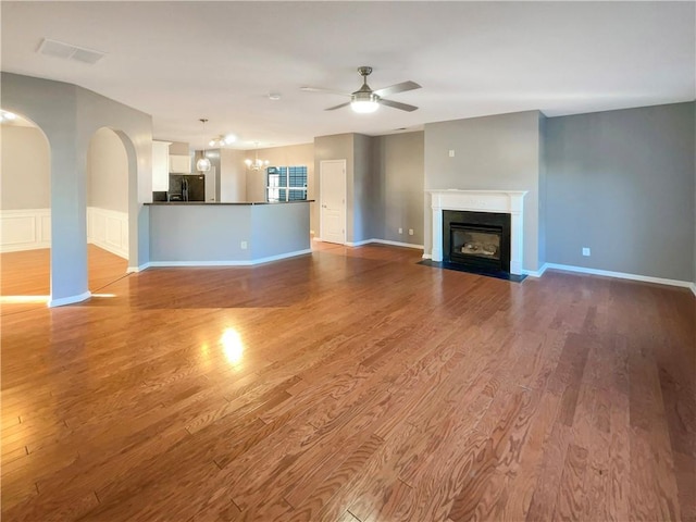 unfurnished living room with ceiling fan with notable chandelier and light wood-type flooring