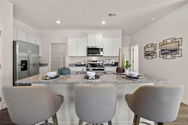 kitchen with appliances with stainless steel finishes, dark hardwood / wood-style flooring, white cabinets, and a kitchen island with sink