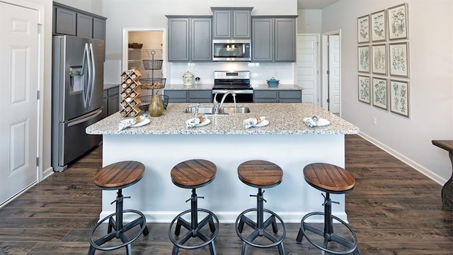 kitchen featuring dark hardwood / wood-style floors, appliances with stainless steel finishes, light stone countertops, an island with sink, and sink