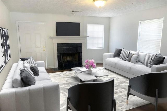 living room with a textured ceiling, dark hardwood / wood-style flooring, and a tiled fireplace