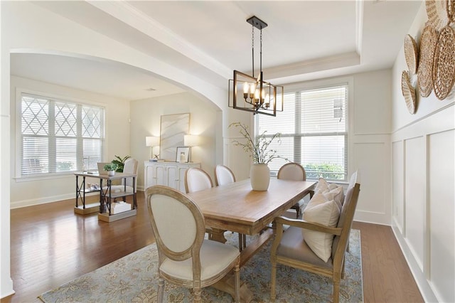 dining room with arched walkways, a decorative wall, a raised ceiling, and wood finished floors