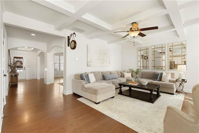 living area featuring arched walkways, beam ceiling, coffered ceiling, and wood finished floors