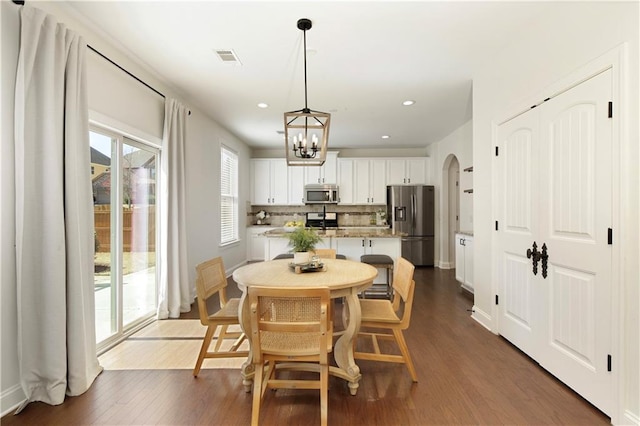 dining area featuring visible vents, baseboards, an inviting chandelier, arched walkways, and dark wood-type flooring