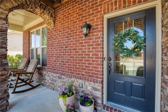 view of exterior entry with brick siding, crawl space, and a porch