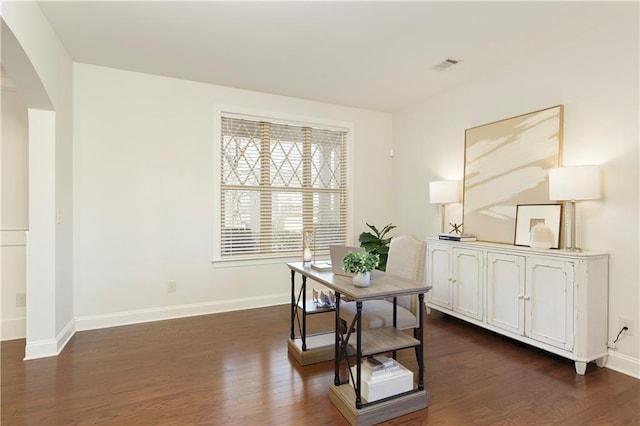 office area with dark wood-style floors, visible vents, arched walkways, and baseboards