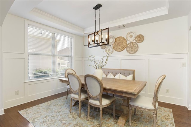 dining room with dark wood-style floors, a decorative wall, and a tray ceiling