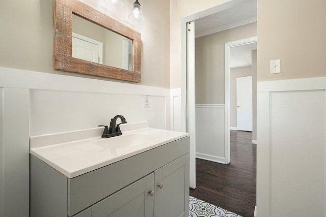 bathroom with vanity, crown molding, a textured ceiling, a wainscoted wall, and wood finished floors