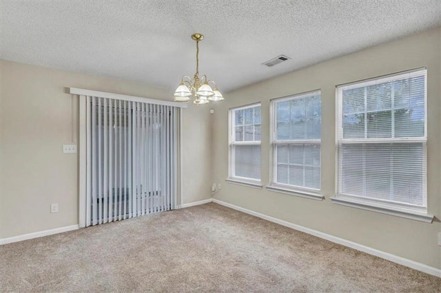 empty room with carpet flooring, a textured ceiling, and a chandelier