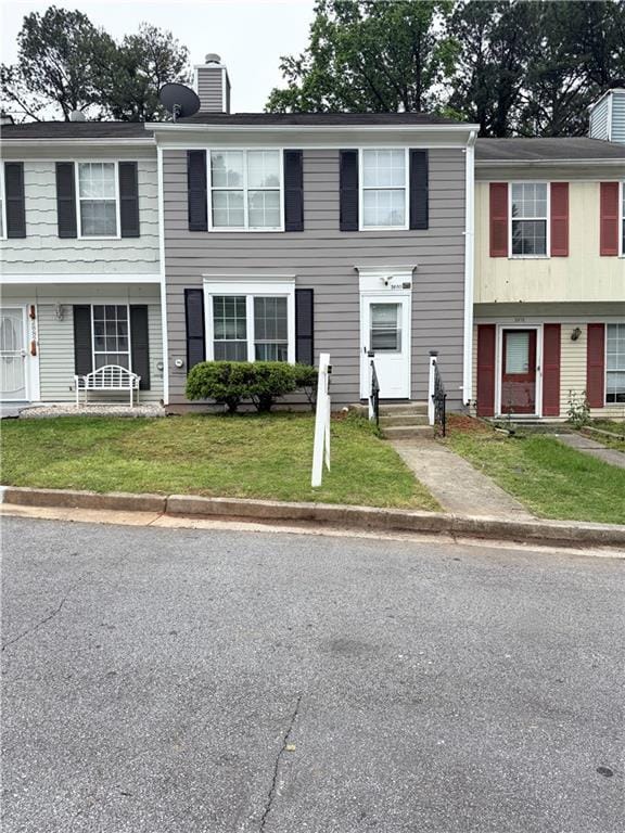 townhome / multi-family property with a front yard, entry steps, and a chimney