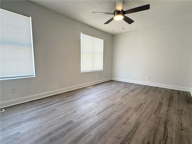 empty room featuring dark wood-style floors, visible vents, a ceiling fan, and baseboards