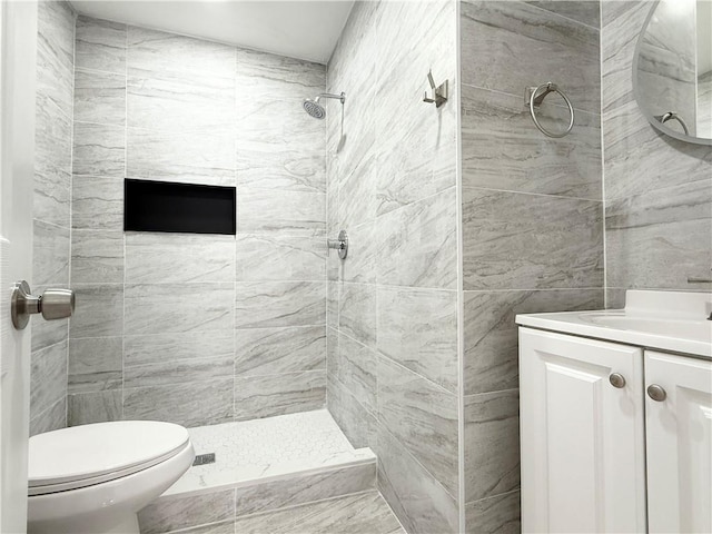 full bath with toilet, tile walls, tiled shower, and vanity