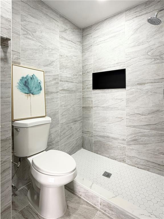 bathroom with a tile shower and toilet