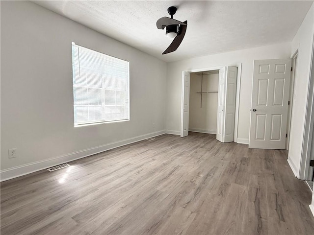 unfurnished bedroom with a closet, ceiling fan, visible vents, baseboards, and wood finished floors