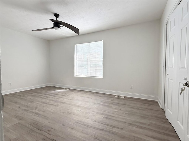 unfurnished bedroom featuring a closet, a ceiling fan, visible vents, baseboards, and wood finished floors