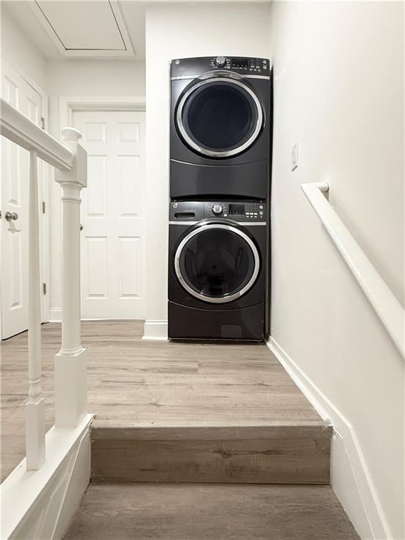 washroom with stacked washing maching and dryer, wood finished floors, and baseboards