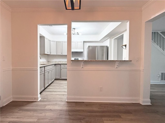 kitchen featuring a sink, visible vents, freestanding refrigerator, baseboards, and wood finished floors
