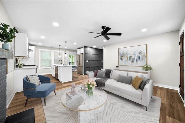 living room featuring sink, a fireplace, ceiling fan, and light wood-type flooring