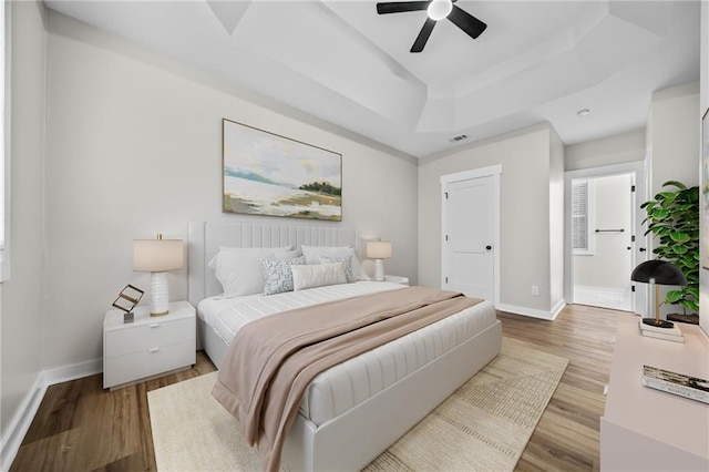 bedroom featuring ceiling fan, light hardwood / wood-style flooring, and a raised ceiling