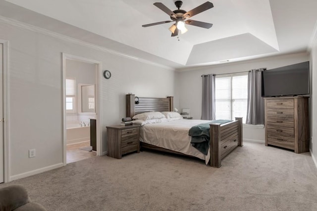 carpeted bedroom with a tray ceiling, ornamental molding, ceiling fan, and ensuite bathroom