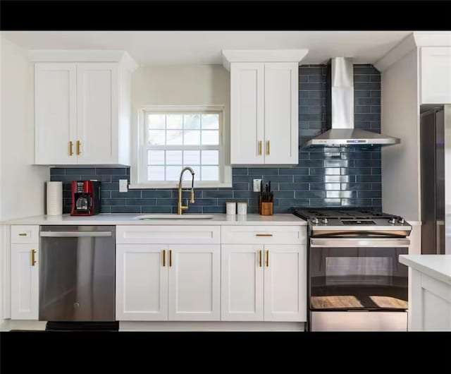 kitchen featuring appliances with stainless steel finishes, sink, wall chimney exhaust hood, white cabinets, and decorative backsplash