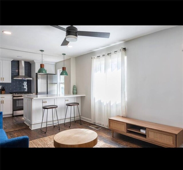 kitchen with appliances with stainless steel finishes, a kitchen bar, kitchen peninsula, white cabinetry, and wall chimney exhaust hood