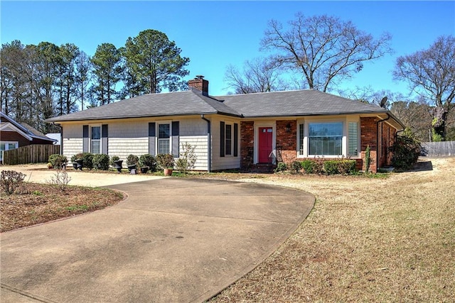 ranch-style home with fence, concrete driveway, a front yard, brick siding, and a chimney