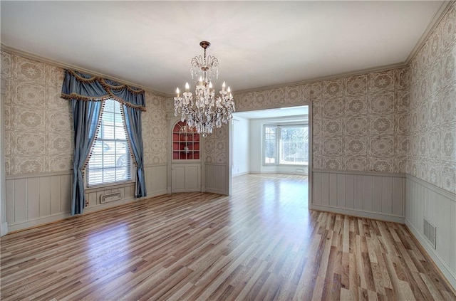 spare room featuring visible vents, wallpapered walls, wainscoting, light wood finished floors, and a chandelier