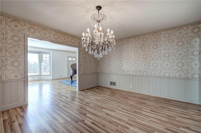 spare room with light wood-type flooring, a wainscoted wall, visible vents, wallpapered walls, and a chandelier