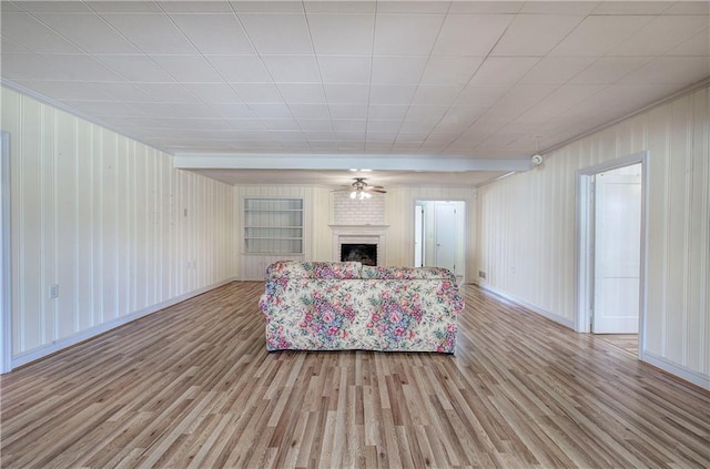 unfurnished living room featuring ceiling fan, a brick fireplace, baseboards, and light wood-style floors