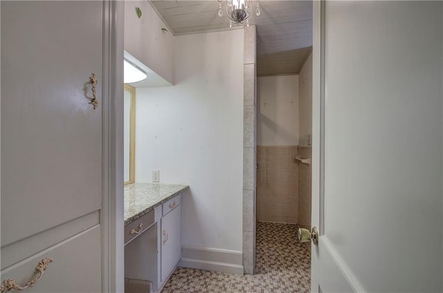 bathroom with tile patterned floors, baseboards, tiled shower, and vanity