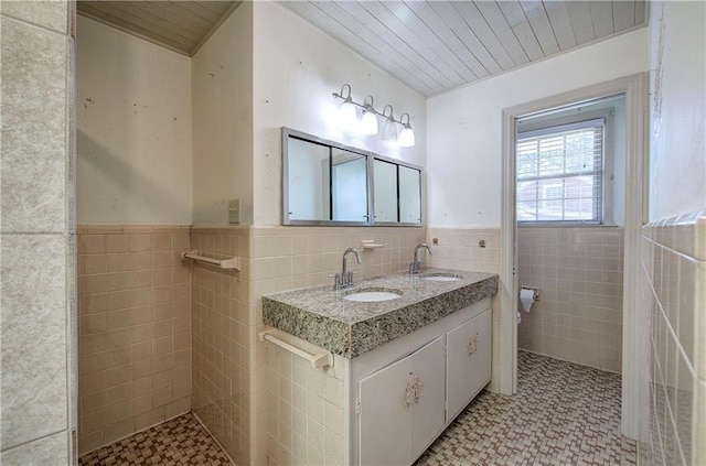 full bathroom with a sink, toilet, tile walls, and wainscoting