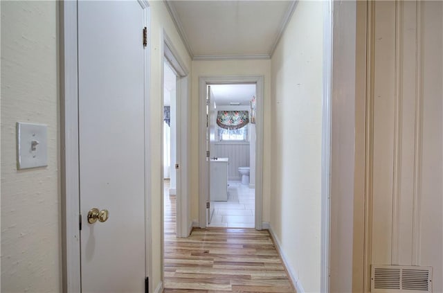 hall with visible vents, baseboards, crown molding, and light wood-style floors