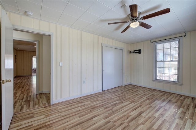 unfurnished bedroom featuring a closet, baseboards, light wood-style floors, and a ceiling fan