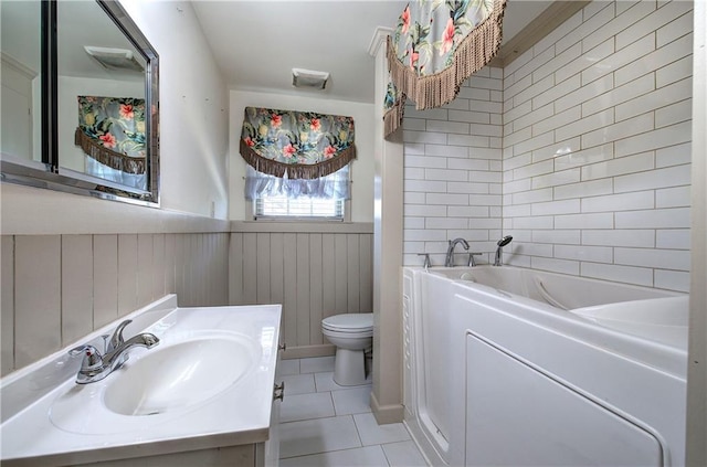 full bath featuring tile patterned flooring, a wainscoted wall, a washtub, toilet, and vanity