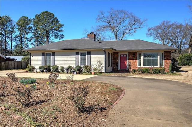 ranch-style house featuring driveway, brick siding, a chimney, and fence