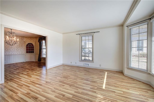 unfurnished room featuring wallpapered walls, ornamental molding, wainscoting, light wood-type flooring, and a chandelier