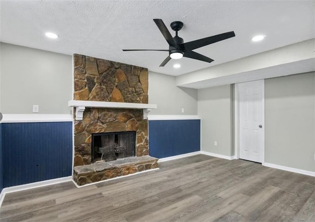 unfurnished living room with a textured ceiling, wood finished floors, and a stone fireplace