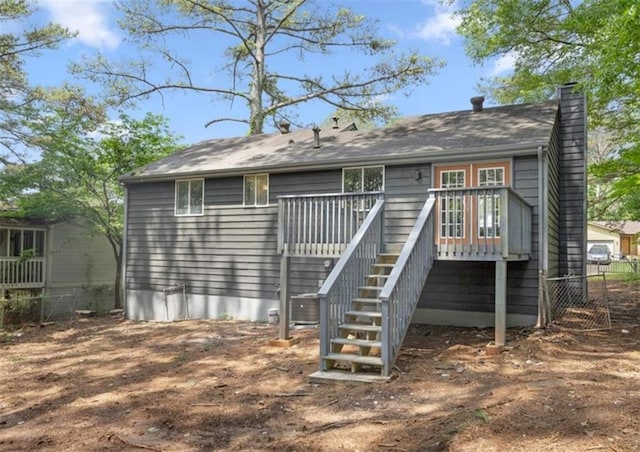 rear view of house with fence, a chimney, a wooden deck, and stairs