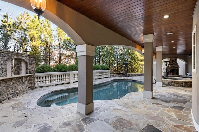 view of swimming pool with a patio area, a hot tub, and an outdoor stone fireplace