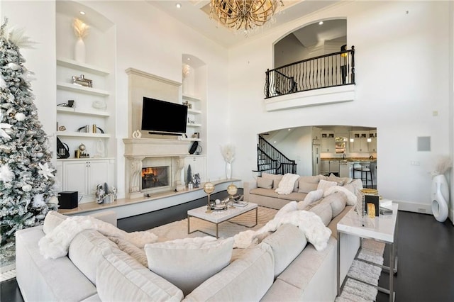 living room featuring a high ceiling, crown molding, built in features, a notable chandelier, and light hardwood / wood-style floors