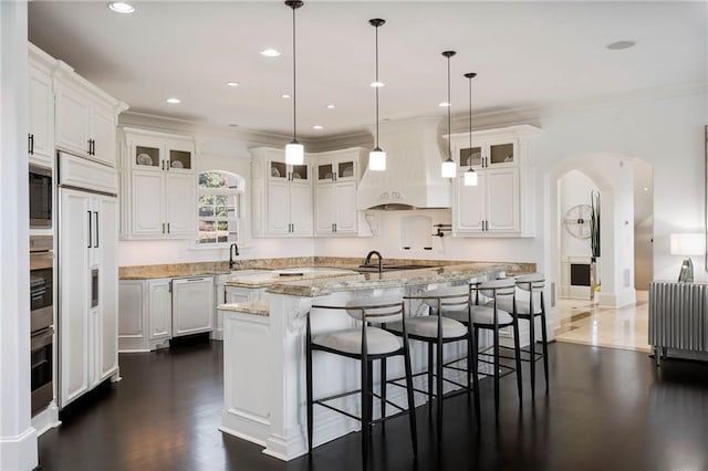 kitchen with white cabinets, light stone counters, a kitchen island with sink, and hanging light fixtures