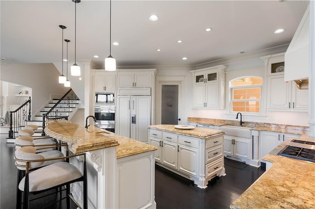 kitchen with a center island with sink, white cabinets, built in appliances, light stone countertops, and decorative light fixtures