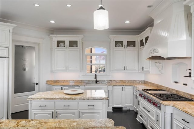 kitchen featuring premium range hood, light stone counters, stainless steel gas cooktop, white cabinetry, and hanging light fixtures