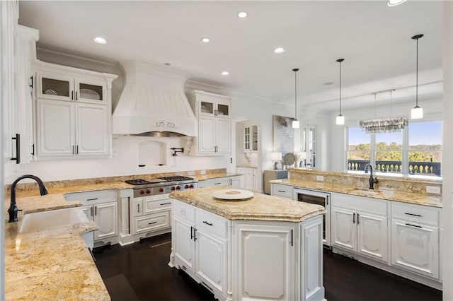 kitchen featuring sink, a kitchen island, stainless steel gas stovetop, white cabinets, and custom exhaust hood