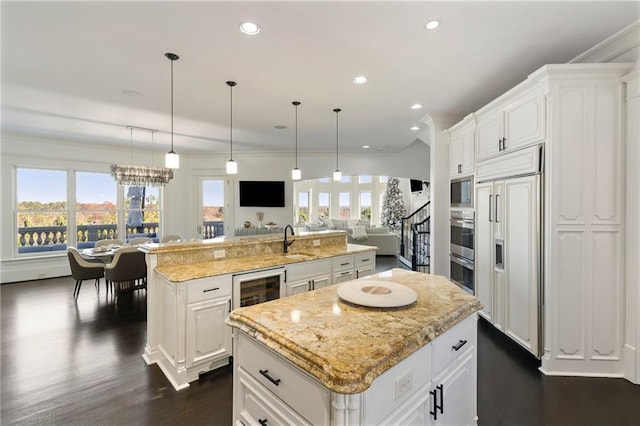 kitchen featuring sink, hanging light fixtures, built in appliances, a spacious island, and white cabinets