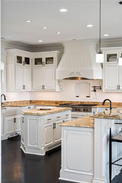 kitchen with white cabinetry, a center island, light stone counters, premium range hood, and pendant lighting