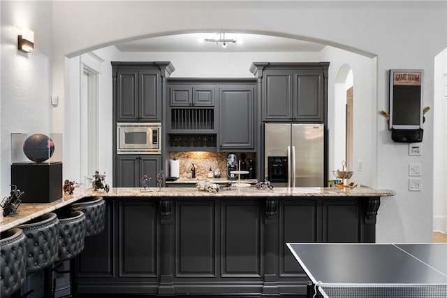 kitchen featuring decorative backsplash, light stone countertops, gray cabinets, and stainless steel appliances