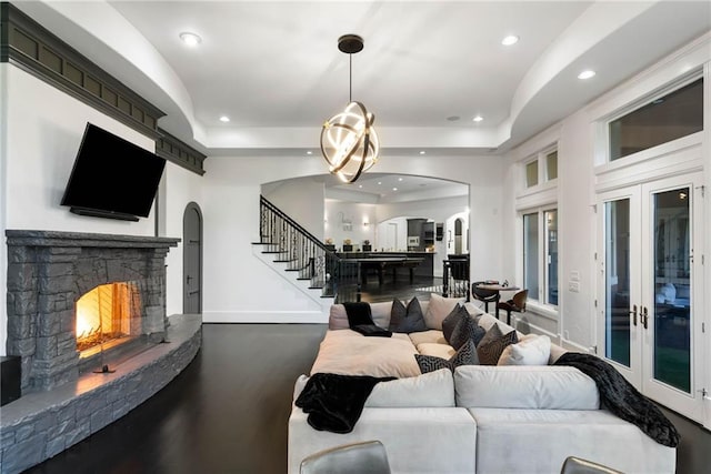 living room with a tray ceiling, a stone fireplace, french doors, and hardwood / wood-style flooring