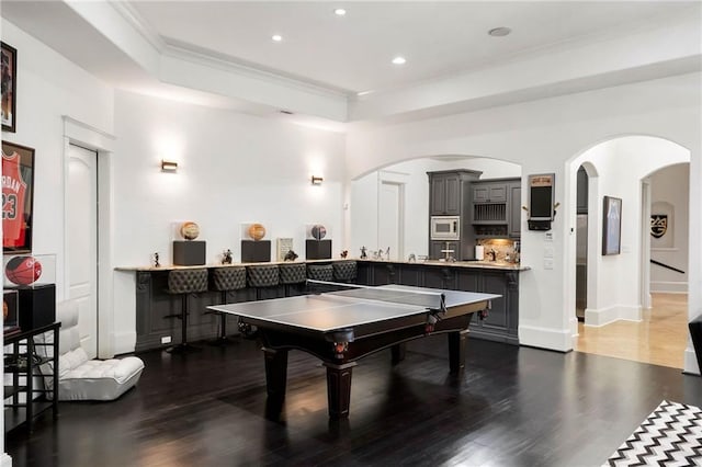 rec room with ornamental molding, a raised ceiling, and dark wood-type flooring